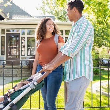 Young mother and father walking with baby daughter in stroller on neighborhood sidewalk