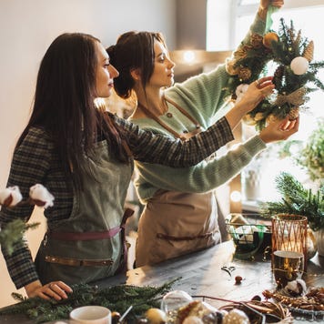 Two women making Christmas wreath using fresh pine branches and festive decorations.