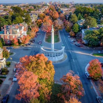 An aerial view above beautiful Fall foliage on Monument Avenue and the skyline of Richmond Virginia in the distance.