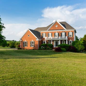 Front of home and garage of large single family modern US house with landscaped gardens and lawn on a warm sunny summers day