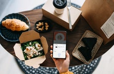 Flat lay of woman's hand holding smartphone with takeaway food ordering mobile app, making mobile payment with credit card, with assorted takeaway dishes served on coffee table. Eating at home and technology concept