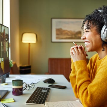 Businesswoman with headphones smiling during video conference. Multiracial male and female professionals are attending online meeting. They are discussing business strategy.