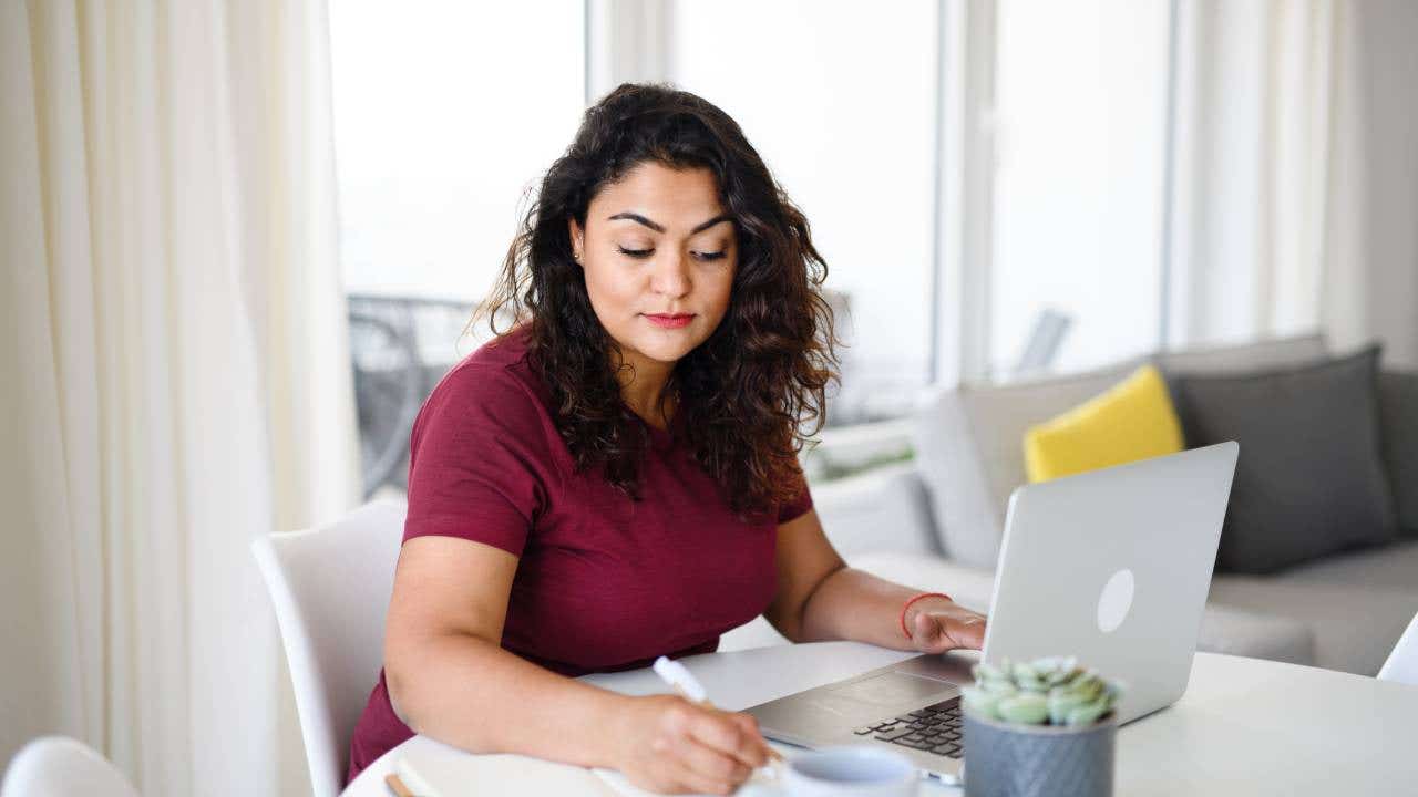 Portrait of young woman with laptop working indoors, home office concept.