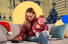 female holding a baby while sitting on a couch using a calculator