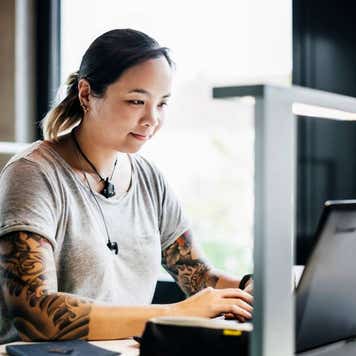 A young woman sitting at a desk and working on her laptop in a public library.