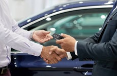 Salesman giving car keys to customer and shaking his hand.