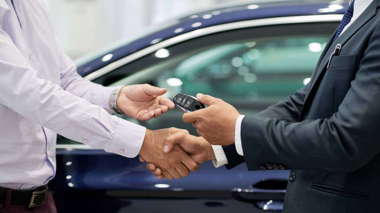 Salesman giving car keys to customer and shaking his hand.