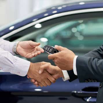 Salesman giving car keys to customer and shaking his hand.