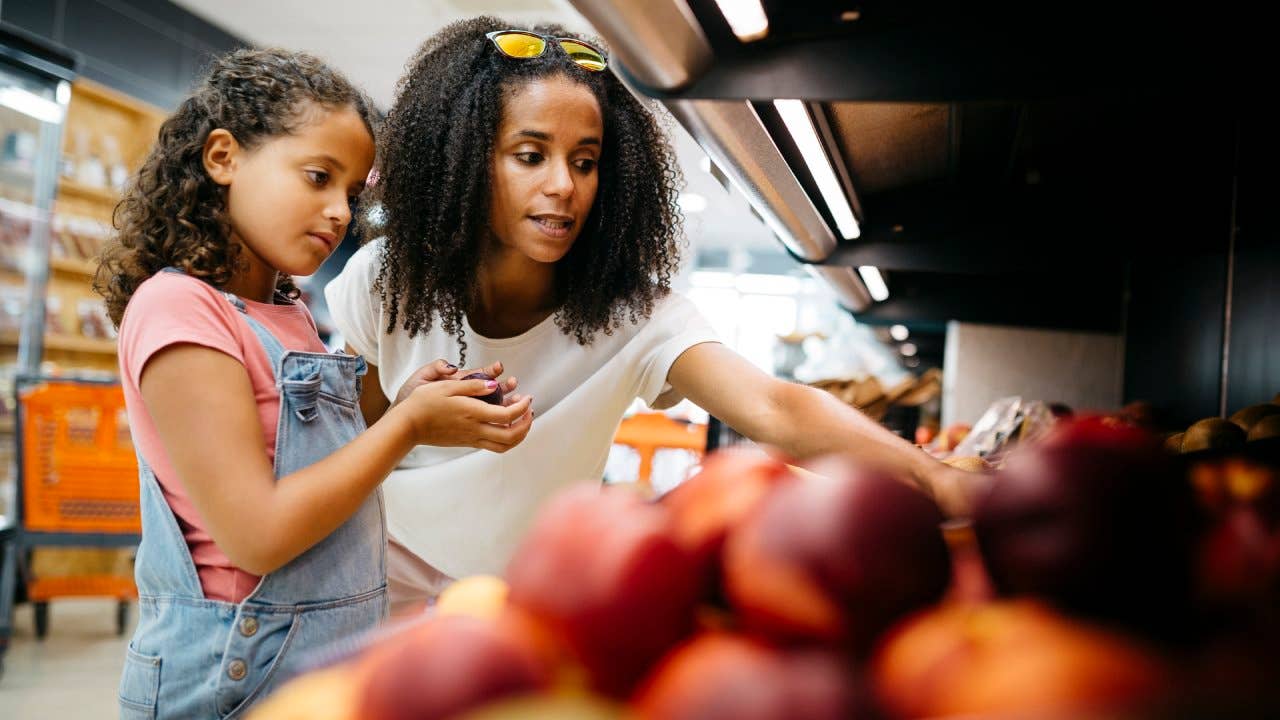 Black single mother and her daughter selecting fruits and vegetables from shelf while shopping in a supermarket