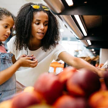 Black single mother and her daughter selecting fruits and vegetables from shelf while shopping in a supermarket