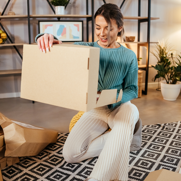 Young adult woman sits in the living room and opens a package