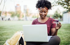 Portrait of a beautiful young African American woman sitting on the grass in the park and shopping online.