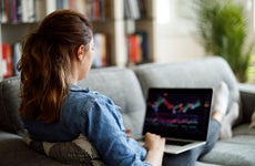 Woman looking at financial graphs on her laptop while sitting on a couch