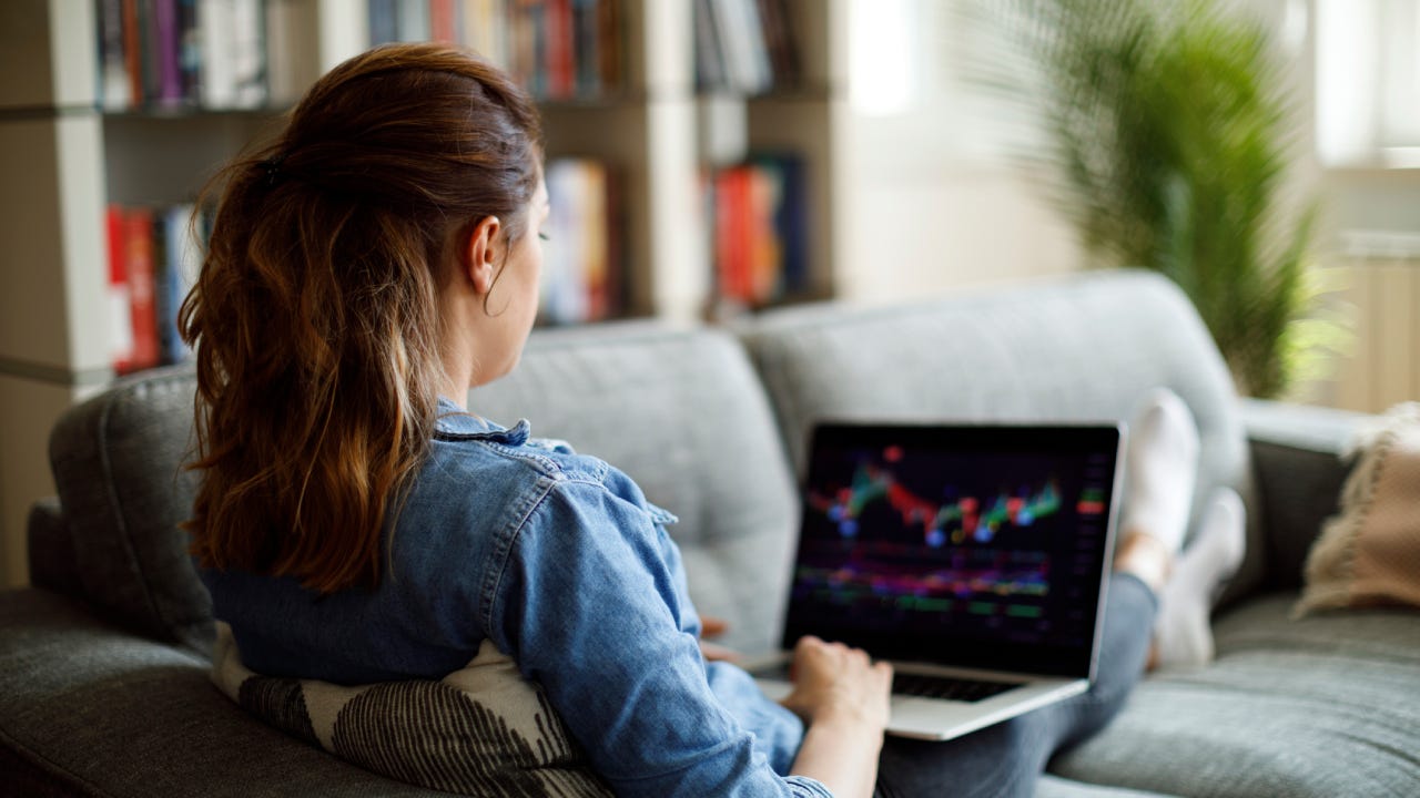 Woman looking at financial graphs on her laptop while sitting on a couch