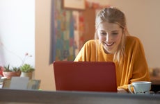 Person in orange shirt sitting at table smiling at red laptop