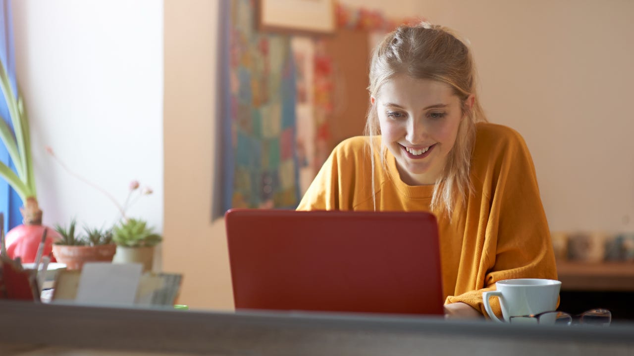 Person in orange shirt sitting at table smiling at red laptop