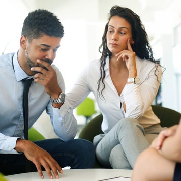 Two well dressed people looking pensive in a car dealership