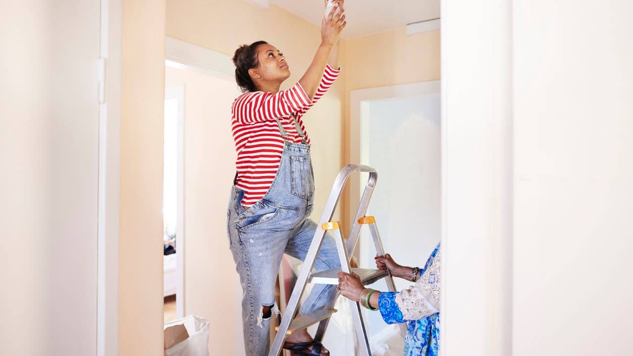 Woman changing light bulb while mother-in-law holding ladder
