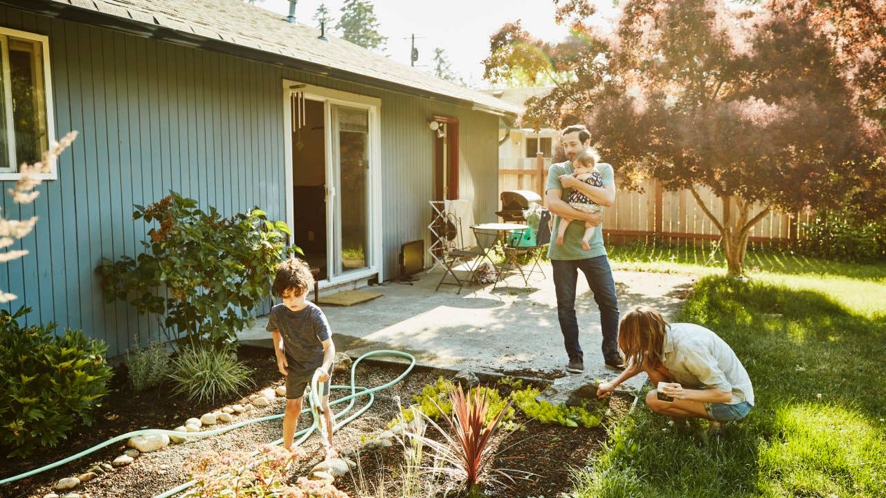 Family watering garden in backyard on summer morning