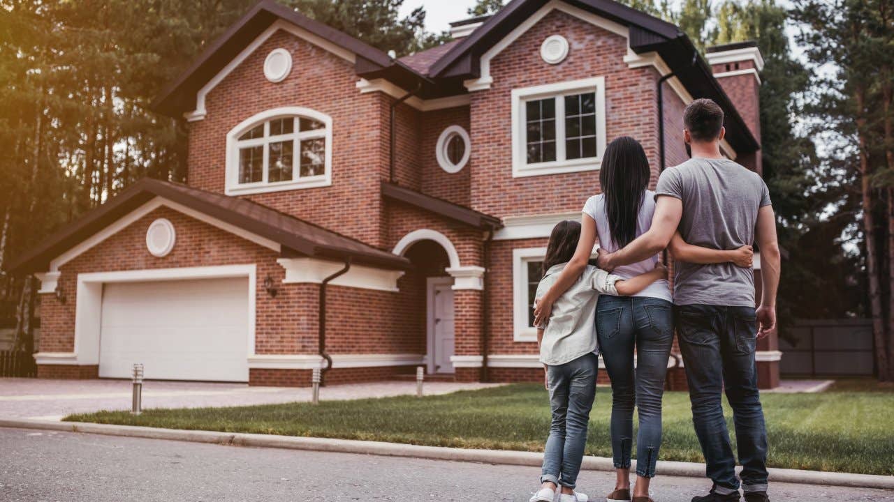 Back view of happy family is standing near their modern house and hugging