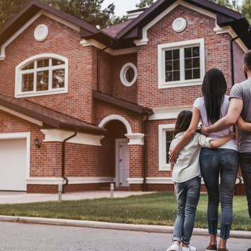 Back view of happy family is standing near their modern house and hugging
