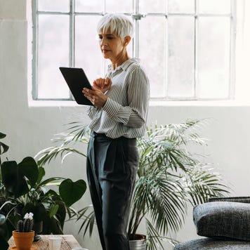 Serious businesswoman reading business report on her tablet while standing in a living room.