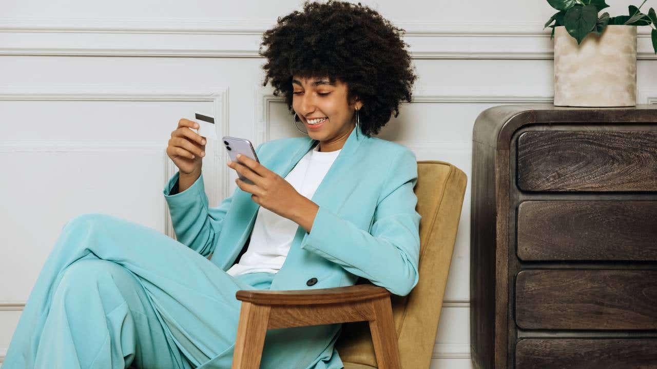 Happy african woman with mobile phone and credit card shopping or taking out a loan online