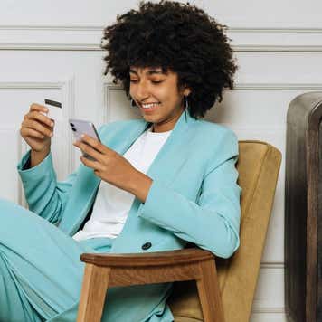 Happy african woman with mobile phone and credit card shopping or taking out a loan online