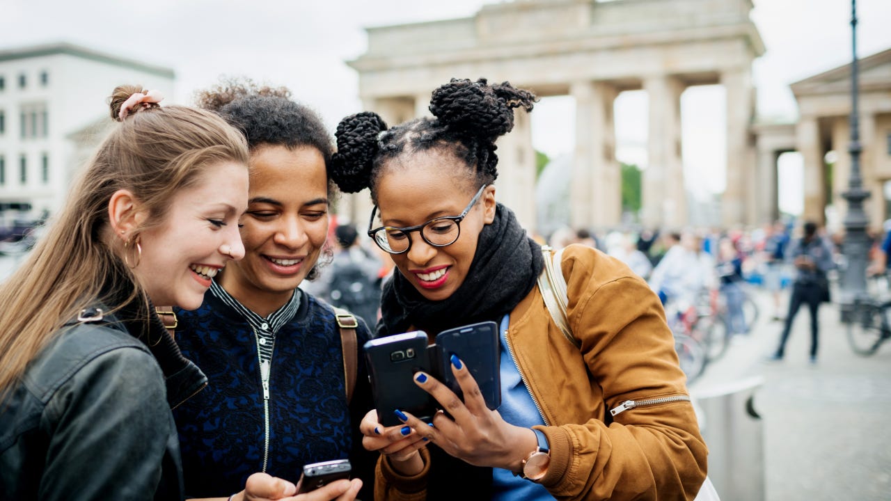 A group of friends travelling together are exploring the local tourist attractions and architecture, they stop for a moment to look over recent photos on their phones.