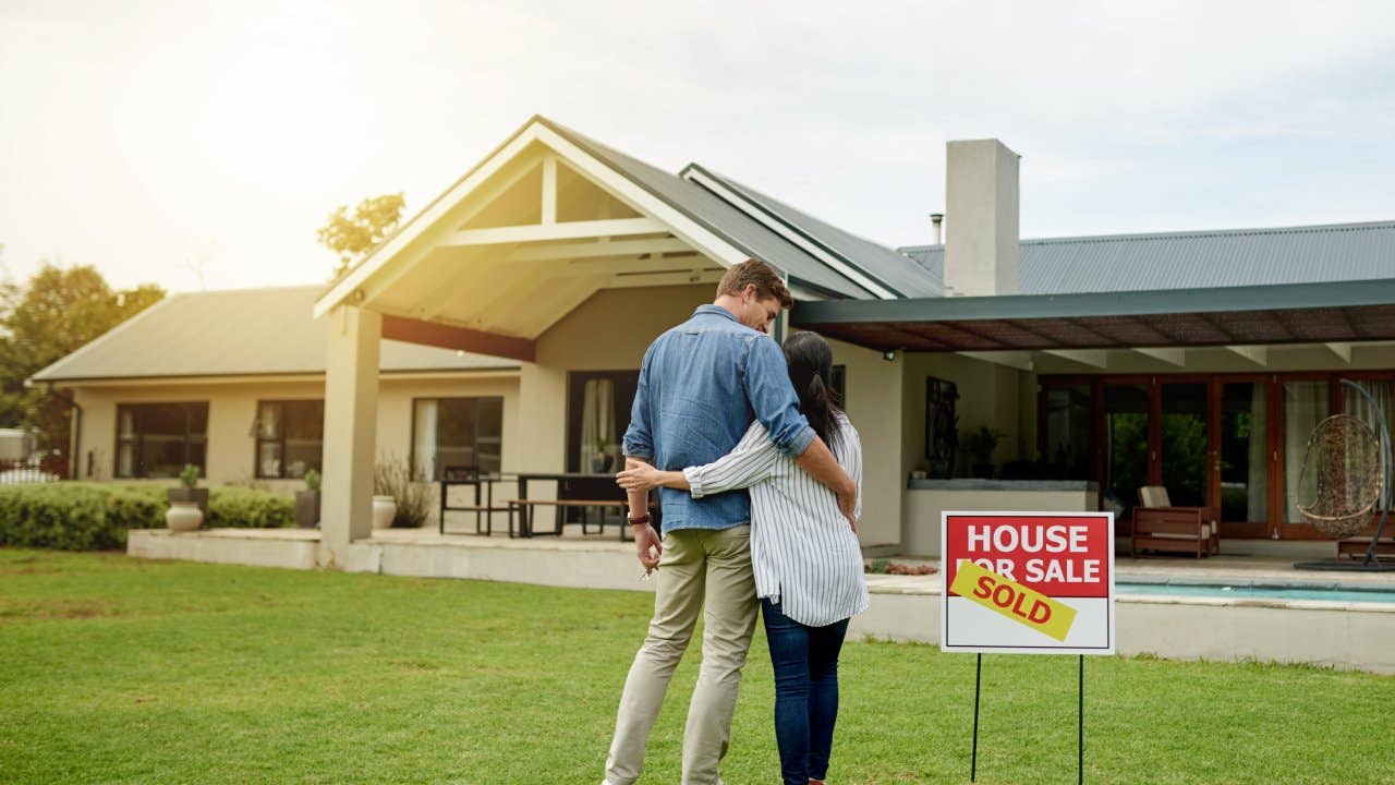 Couple standing next to a real estate sold sign at their new house