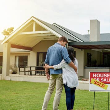Couple standing next to a real estate sold sign at their new house