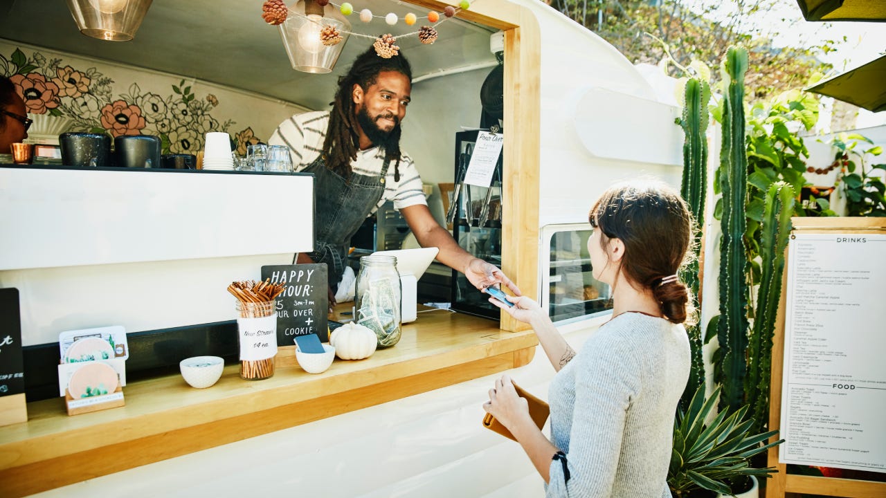 Smiling food truck owner taking credit card for payment from customer - stock photo