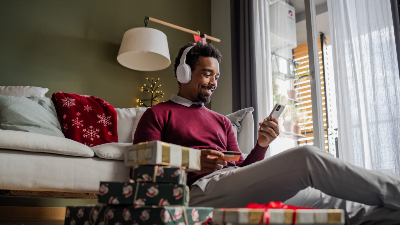 African American man sitting on the floor, using a credit card and smart phone. He is doing online Christmas shopping.