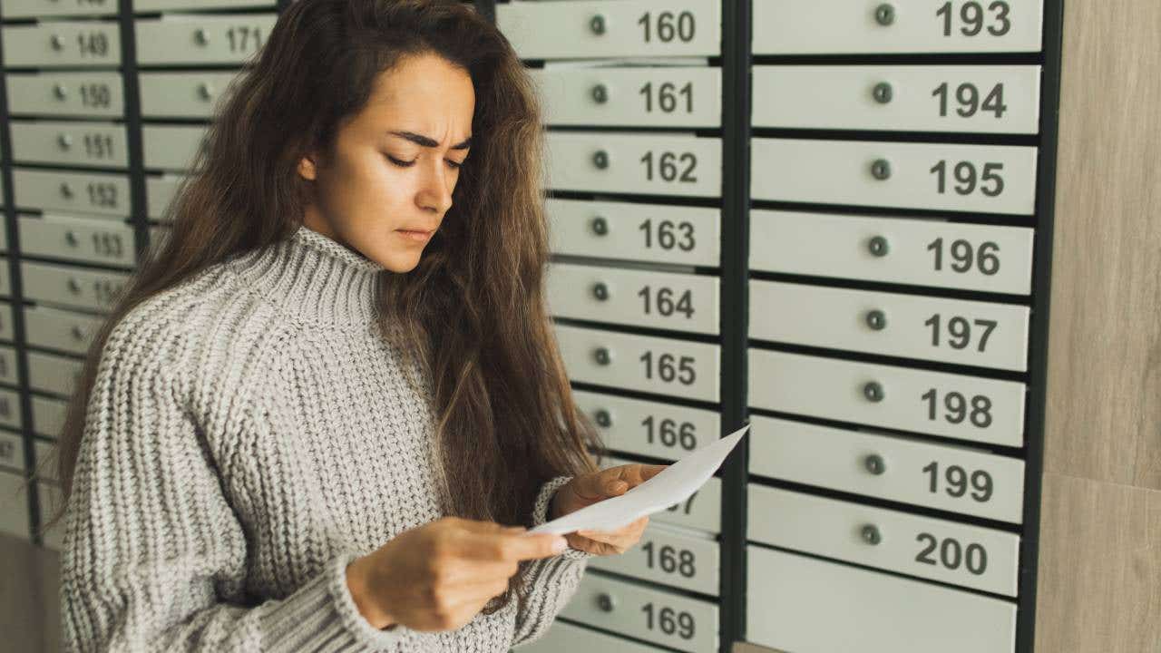 Upset and stressed woman near post box disappointed by bad news and bills from letter mail