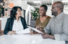 Two business owners, a Black man and a Black woman, discuss loan details with a loan officer.