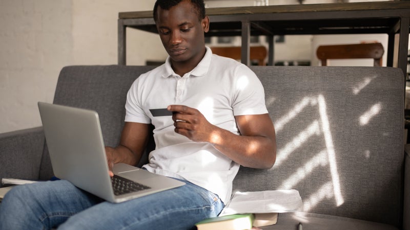 African American student shopping online sitting on sofa - stock photo