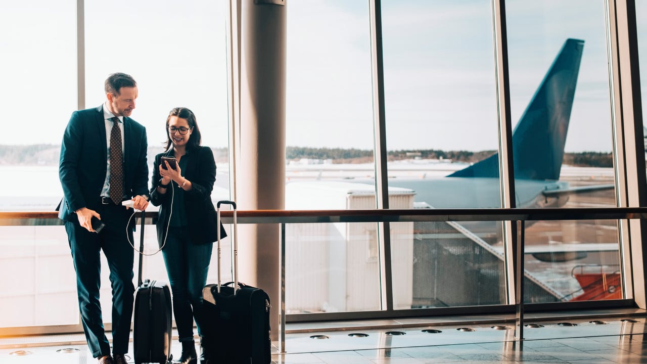 Full length of business couple with luggage using mobile phone in airport