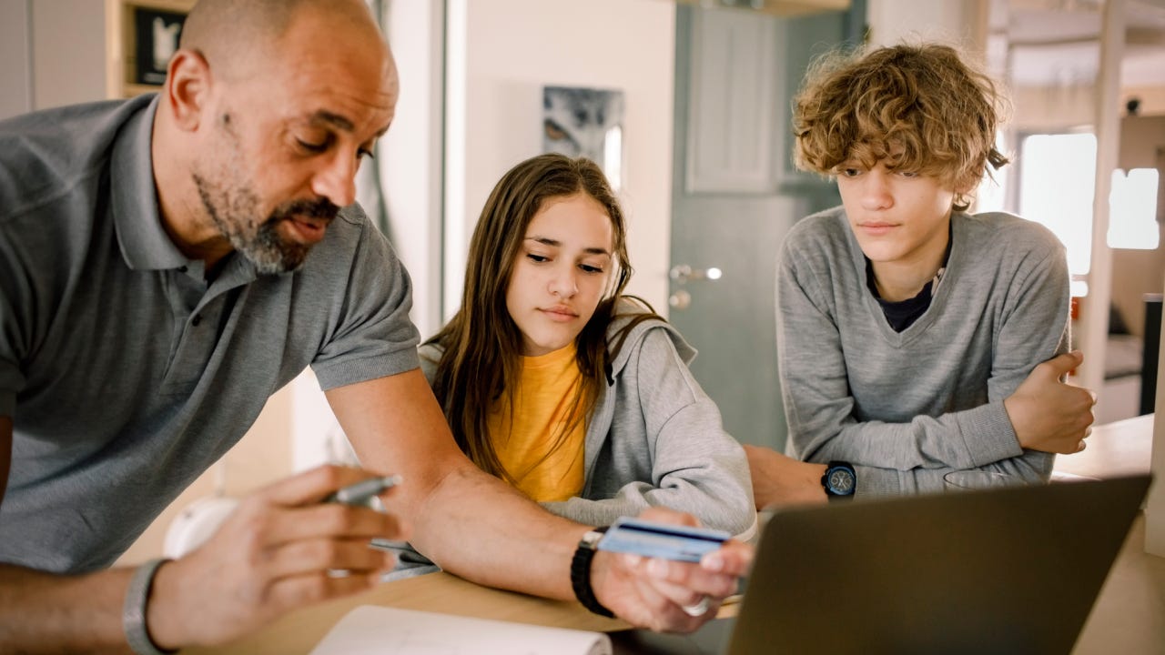 Brother and sister looking at father explaining finance with credit card at kitchen island