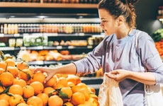 Woman choosing orange at market and using reusable eco bag.