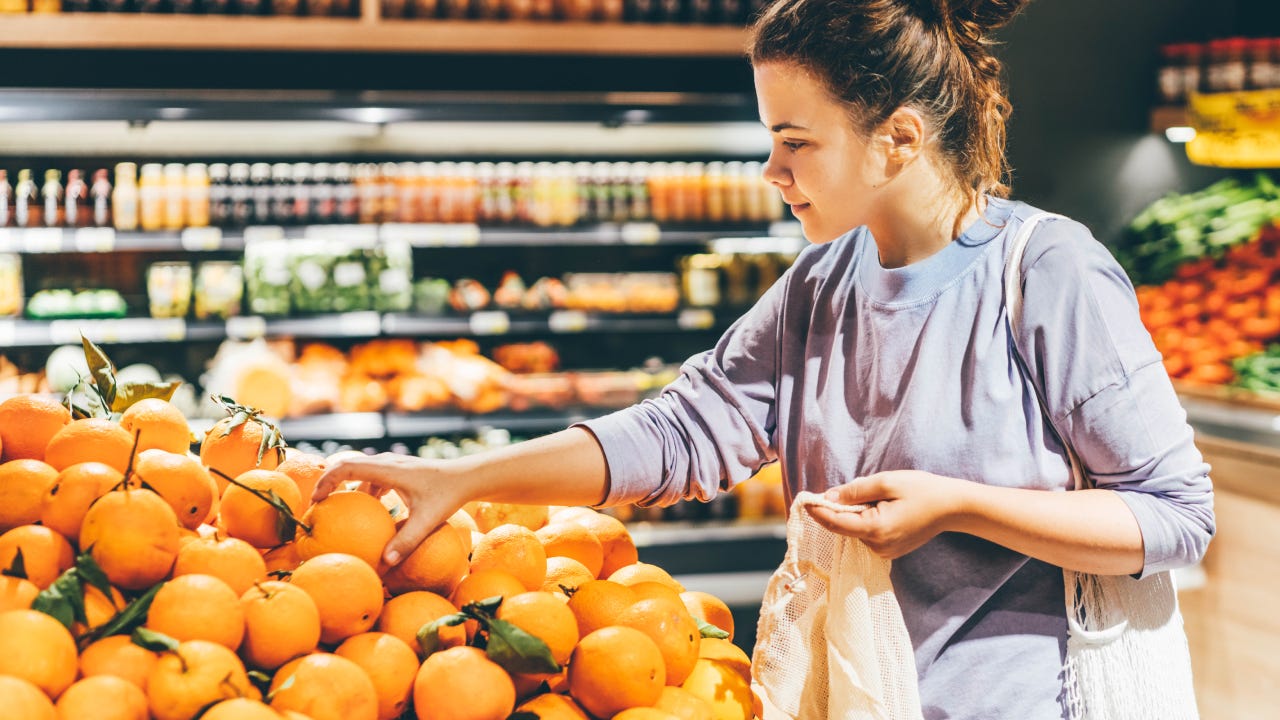 Woman choosing orange at market and using reusable eco bag.