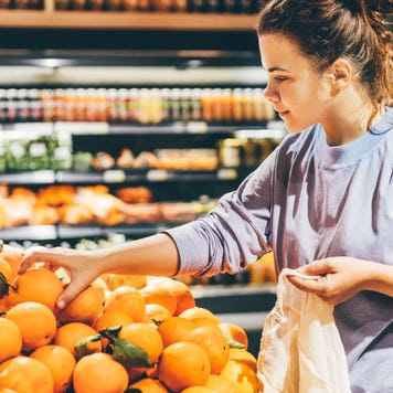 Woman choosing orange at market and using reusable eco bag.