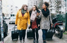 Three Women Walking Down City Street With Rolling Suitcases