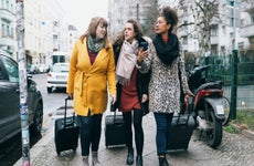 Three Women Walking Down City Street With Rolling Suitcases