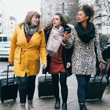 Three Women Walking Down City Street With Rolling Suitcases
