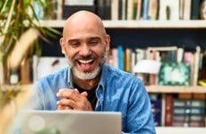 A bald business owner smiles at a laptop screen.