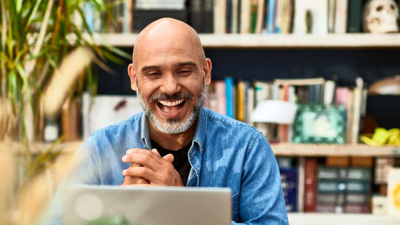 A bald business owner smiles at a laptop screen.