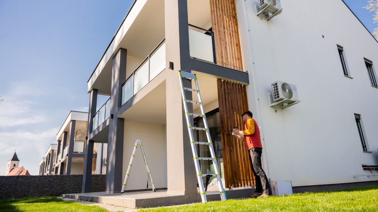 Man painting wooden columns of modern apartment against sky during sunny day