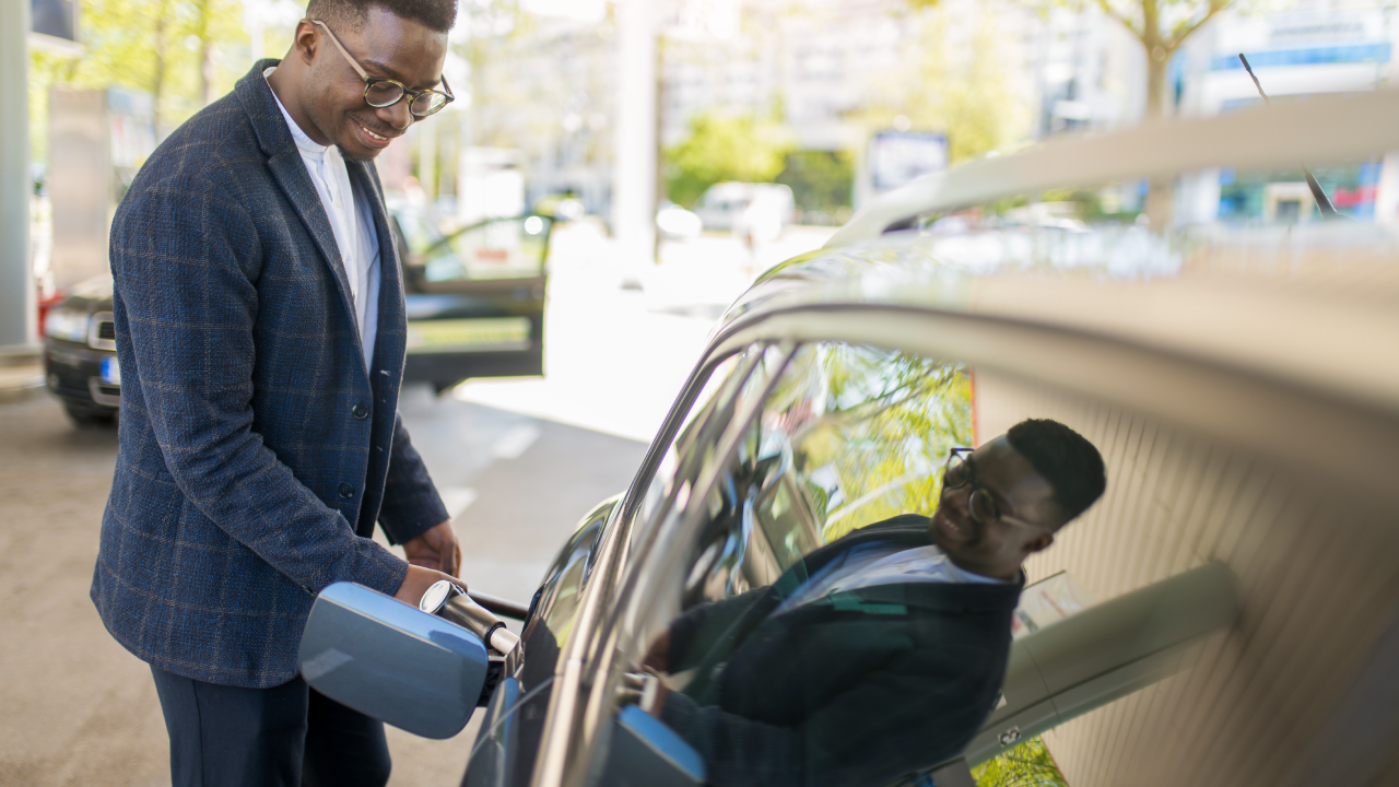 Young African American businessman sipping fuel into his car tank at the gas station.