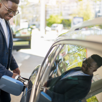 Young African American businessman sipping fuel into his car tank at the gas station.