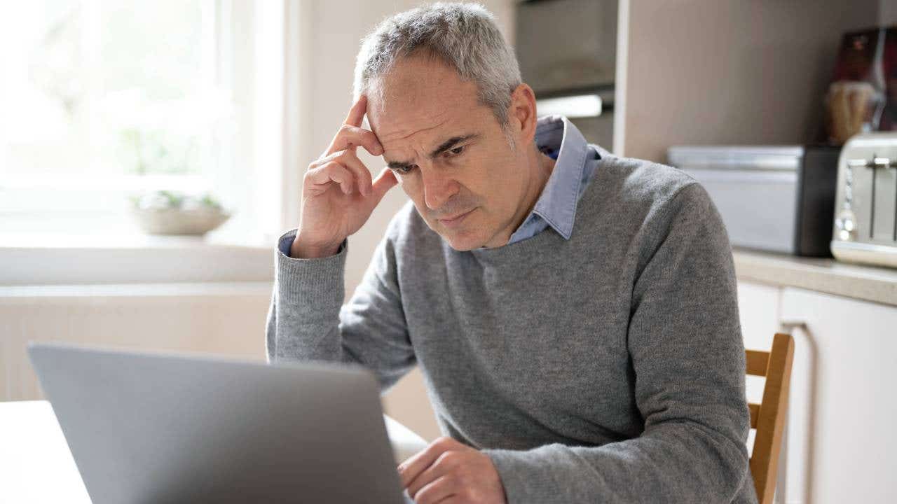 Mature caucasian man in his 50s using laptop looking concerned, puzzled and confused.